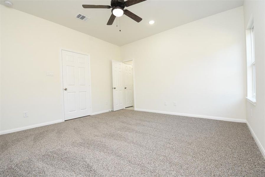 Empty room with beige carpet, white walls, two doors, a window, and a ceiling fan.