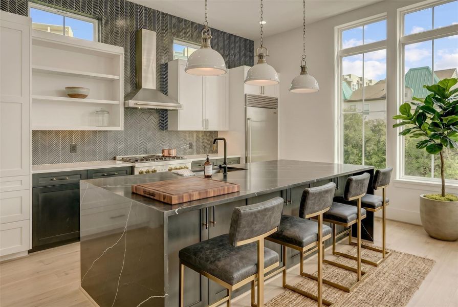 Chef's kitchen with waterfall island, stainless steel appliances, and surrounding windows. Virtually staged photo. Chef's kitchen with waterfall island, stainless steel appliances, and surrounding windows. Virtually staged photo.