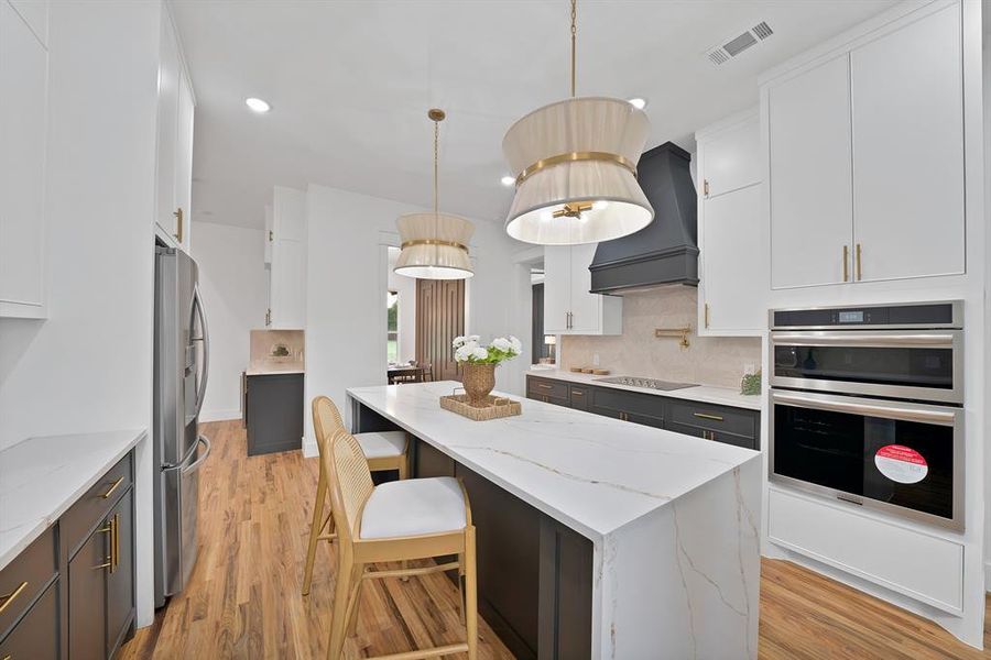 This kitchen features a large center island with a white countertop, two pendant lights, and hardwood flooring