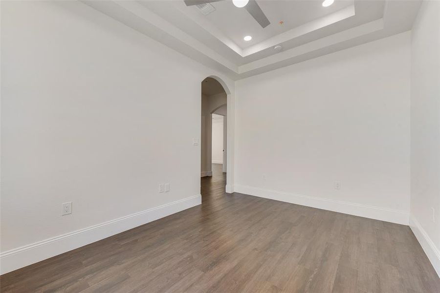 Spacious interior room featuring wood-finish flooring, white baseboards, and a tray ceiling with recessed lighting Spacious interior room featuring wood-finish flooring, white baseboards, and a tray ceiling with recessed lighting