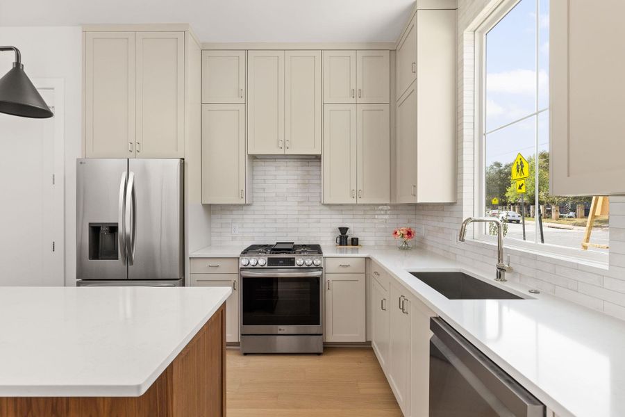 Kitchen featuring stainless steel appliances, decorative backsplash, light stone counters, and light wood finished floors Kitchen featuring stainless steel appliances, decorative backsplash, light stone counters, and light wood finished floors