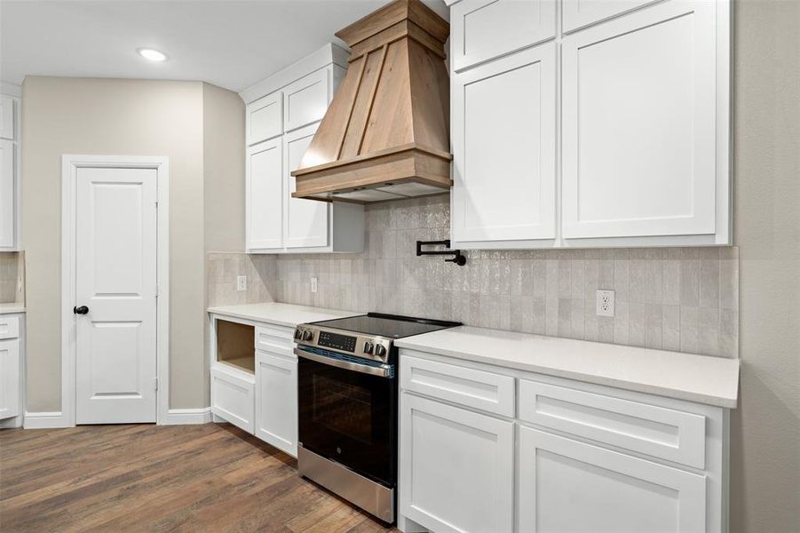 Kitchen with stainless steel electric range, white cabinets, custom range hood, backsplash, and dark wood-style flooring