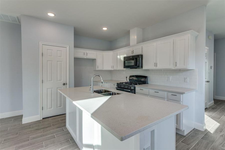 Kitchen featuring black appliances, sink, white cabinets, and a kitchen island with sink