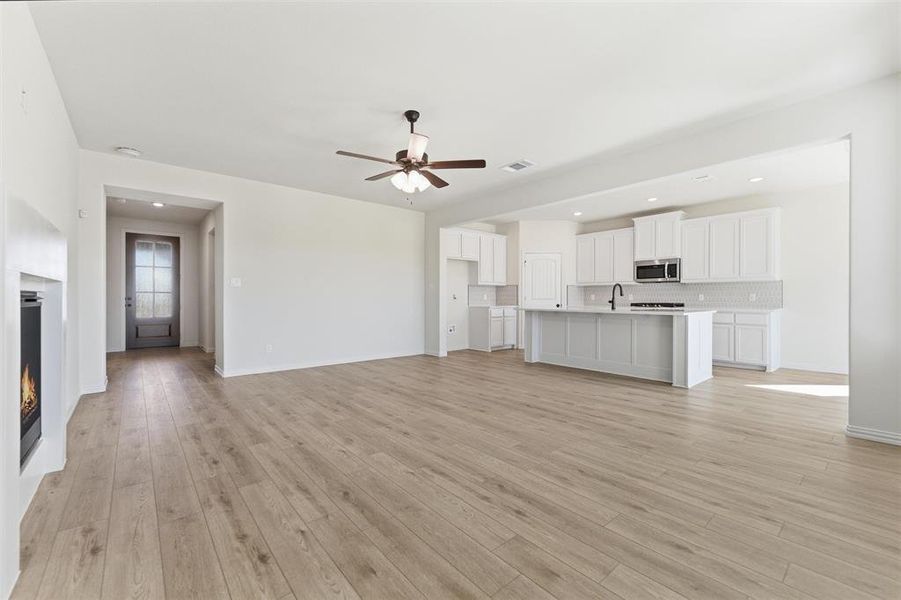 Unfurnished living room featuring a ceiling fan, a warm lit fireplace, light wood-type flooring, and recessed lighting