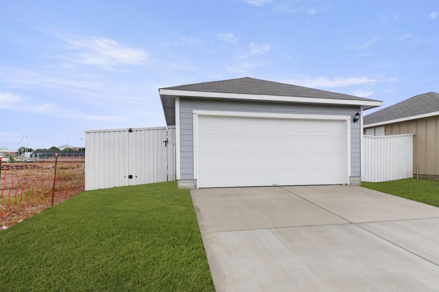 Image of the exterior front of a two car garage with a white door and cement driveway with green grass and a white fence