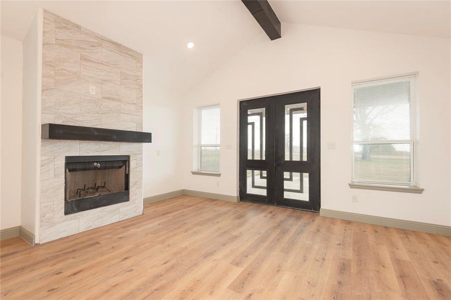 Unfurnished living room with light wood-style flooring, beam ceiling, a fireplace, and high vaulted ceiling
