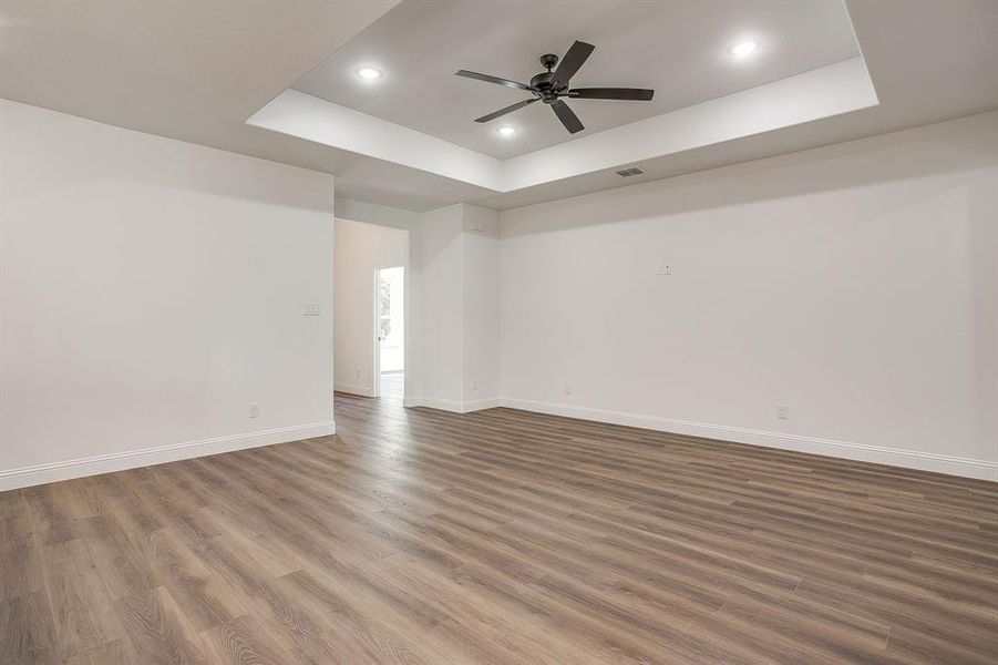 Empty room with a raised ceiling, dark wood finished floors, ceiling fan, and recessed lighting