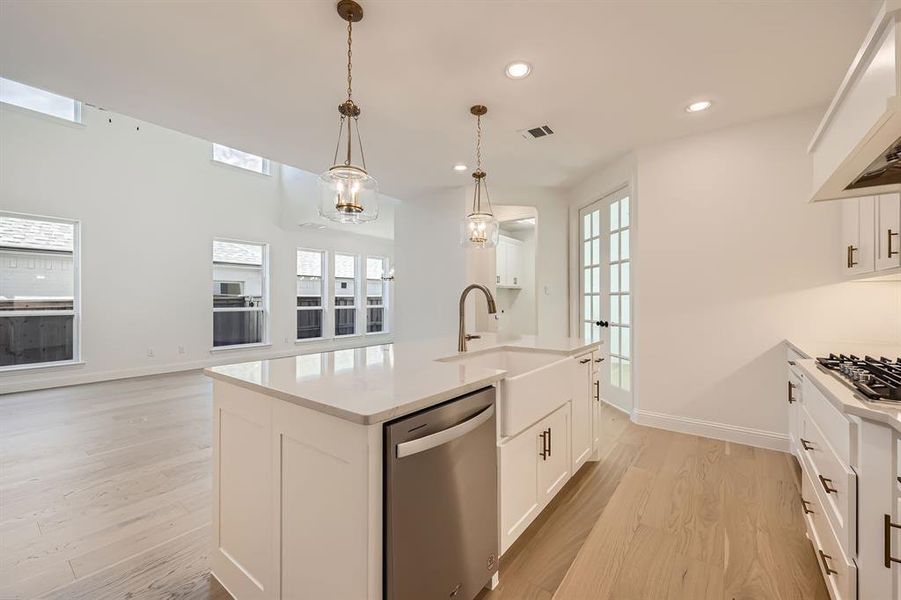 Kitchen featuring pendant lighting, dishwasher, light wood-type flooring, and an island with sink