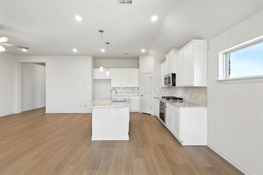 Kitchen featuring tasteful backsplash, pendant lighting, white cabinets, a kitchen island with sink, and recessed lighting Kitchen featuring tasteful backsplash, pendant lighting, white cabinets, a kitchen island with sink, and recessed lighting