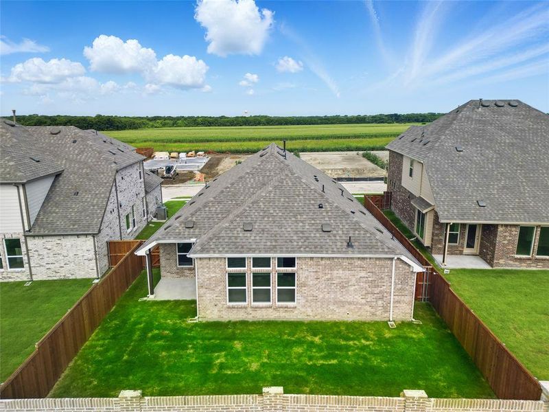 Back of house with brick siding, a view of countryside, roof with shingles, a patio area, and agricultural area