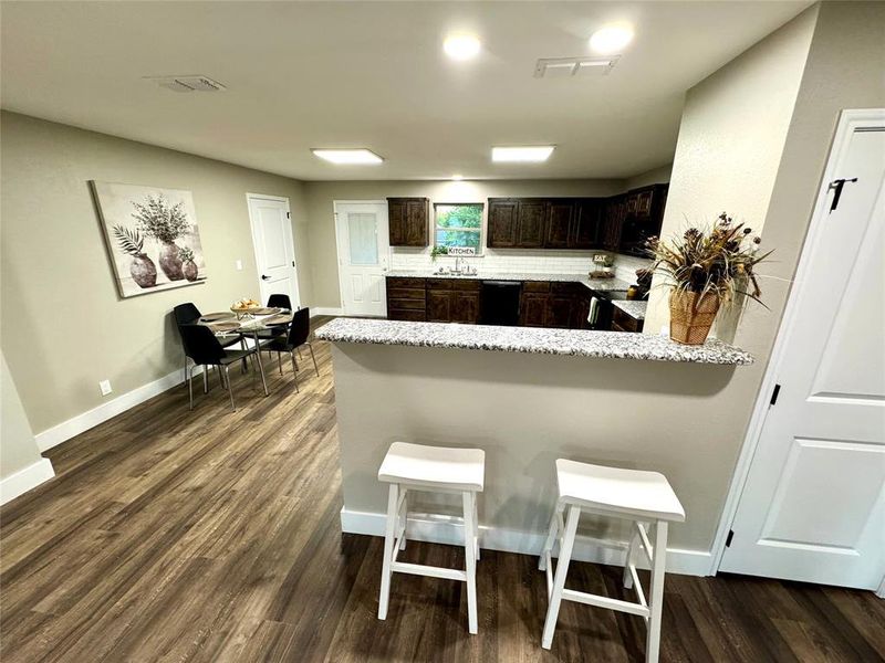 Kitchen featuring dark brown cabinets, a peninsula, dark wood-type flooring, a breakfast bar, and black appliances