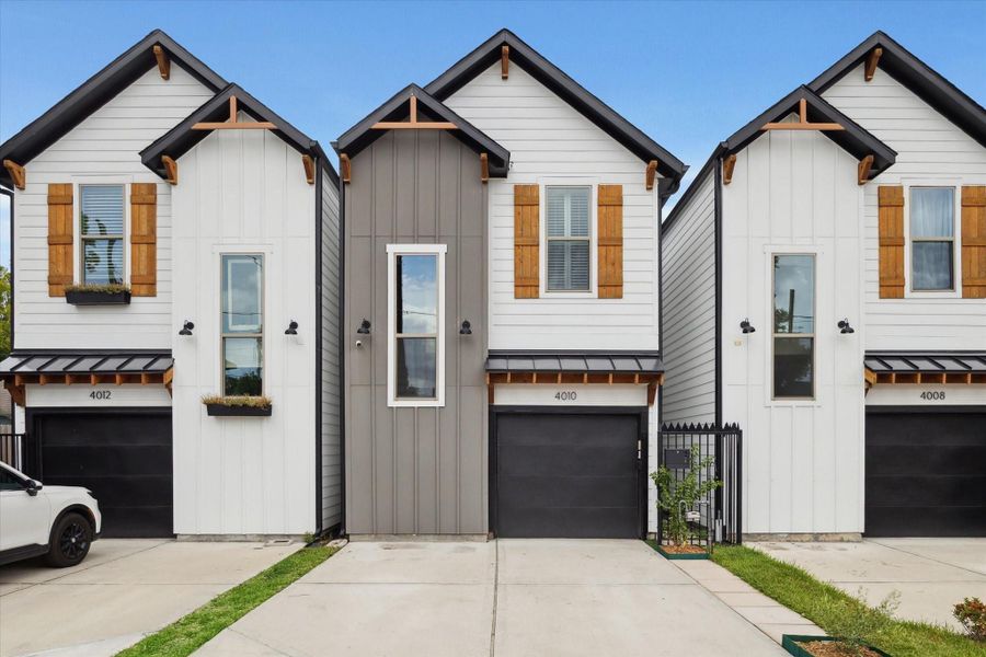 Modern townhouse with a sleek facade, featuring a two-story design, black garage door, and wood accents. The exterior is a mix of white and gray siding with large windows, offering a contemporary and inviting look.