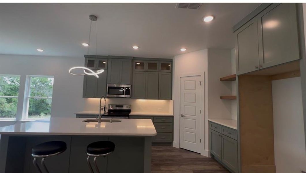 Open-concept kitchen featuring an island with an undermount sink, pendant lighting, stainless steel appliances, and abundant cabinetry with under-cabinet lighting