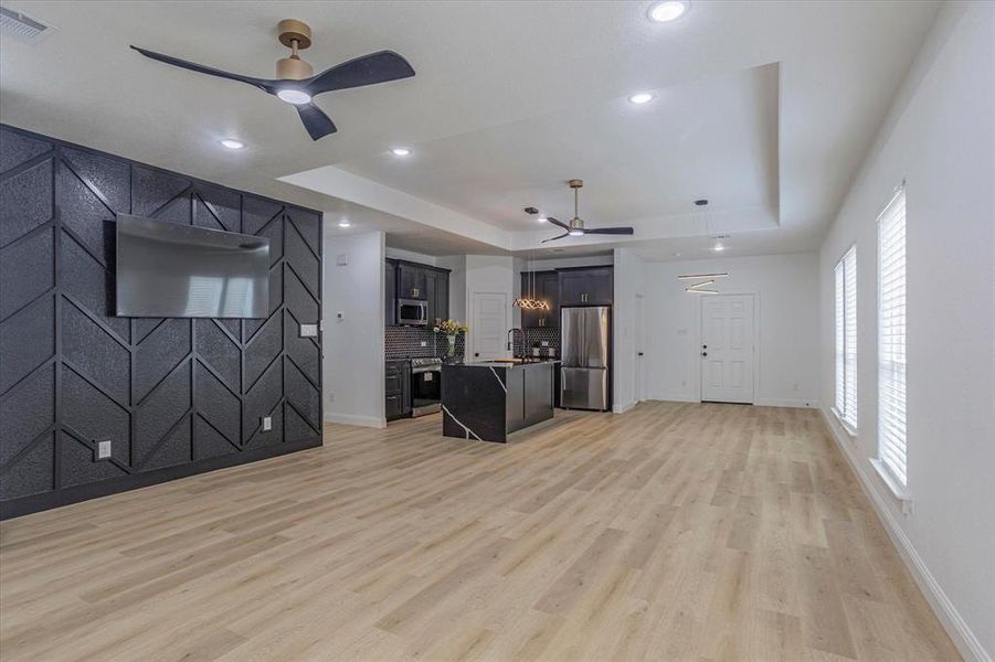 Unfurnished living room with light wood-type flooring, ceiling fan, and a raised ceiling