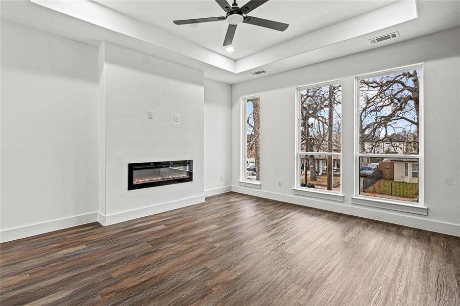 Unfurnished living room featuring dark wood-style floors, a glass covered fireplace, ceiling fan, a tray ceiling, and recessed lighting