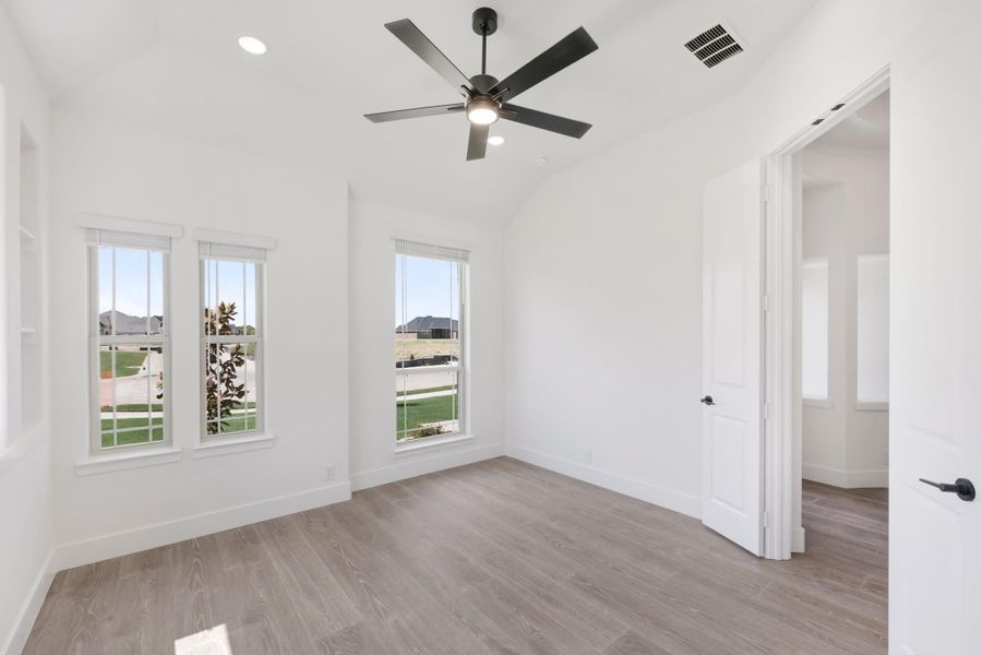 Empty bedroom with vaulted ceiling, black ceiling fan, hardwood floors, and three windows with natural light