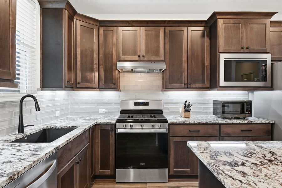 Kitchen with stainless steel appliances, light stone counters, tasteful backsplash, and dark wood finish cabinets