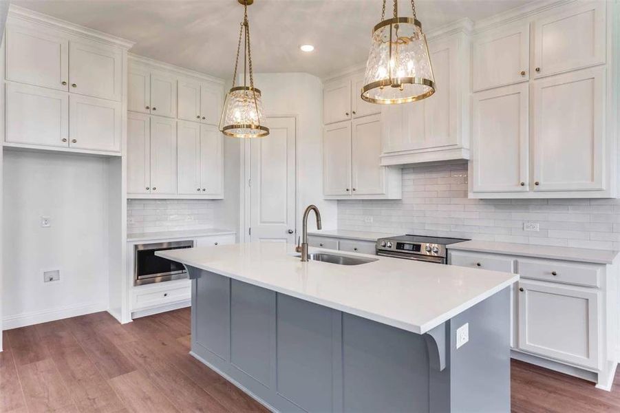 Kitchen featuring gray cabinetry, backsplash, a kitchen island with sink, white cabinetry, and light wood-style flooring Kitchen featuring gray cabinetry, backsplash, a kitchen island with sink, white cabinetry, and light wood-style flooring