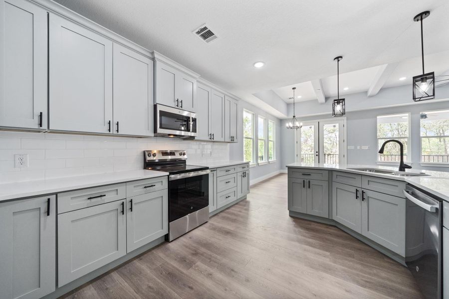 Modern kitchen featuring light gray cabinetry with black hardware, stainless steel appliances, white subway tile backsplash, and wood-finish flooring