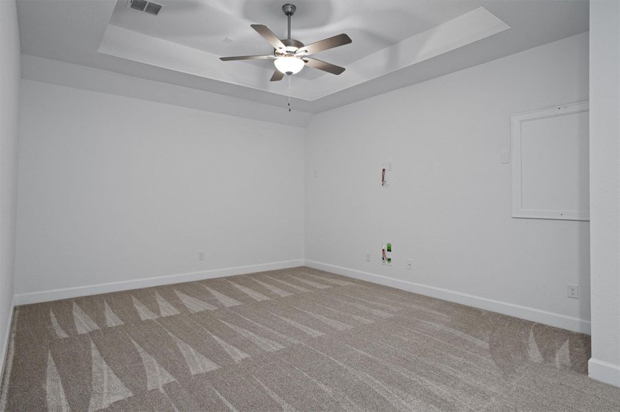 Spacious room featuring a tray ceiling, ceiling fan with integrated lighting, and light-toned patterned carpeting