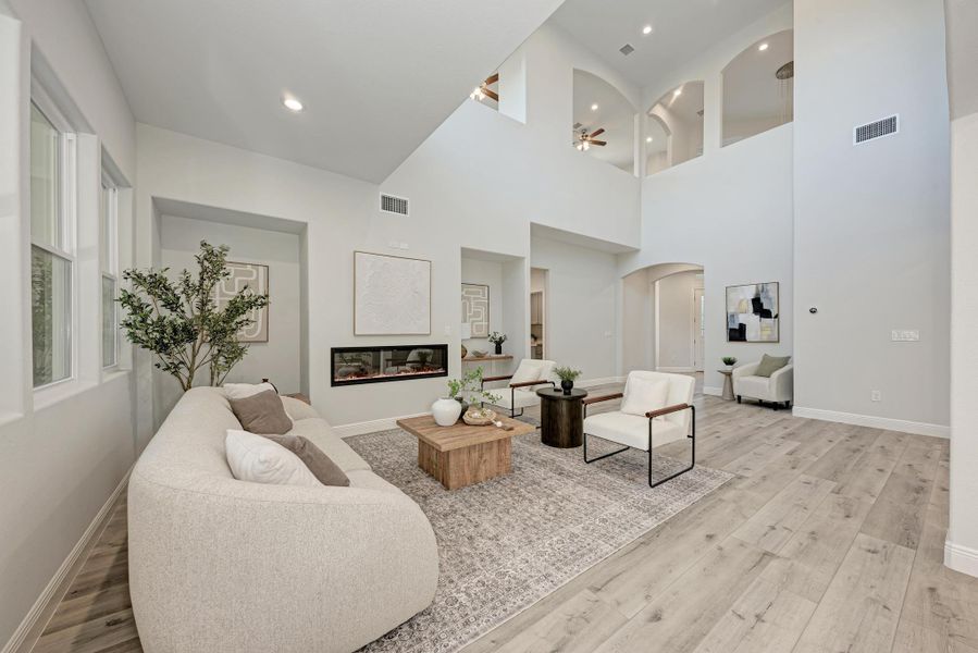 Living room with arched walkways, light wood-style flooring, a ceiling fan, a glass covered fireplace, and recessed lighting