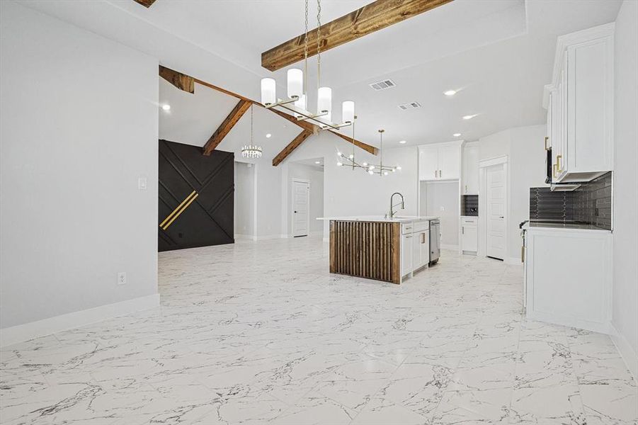 Kitchen with sink, a kitchen island with sink, beam ceiling, white cabinets, and decorative light fixtures