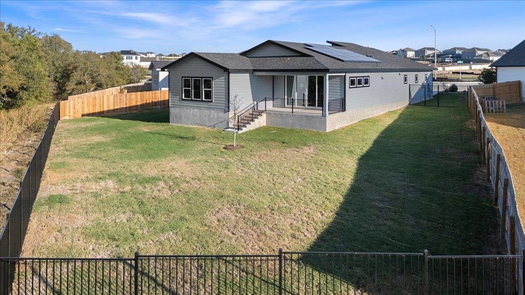 Back of house featuring a fenced backyard, roof mounted solar panels, and a shingled roof Back of house featuring a fenced backyard, roof mounted solar panels, and a shingled roof