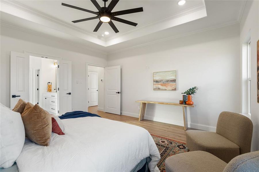 Bedroom featuring a raised ceiling, ceiling fan, ornamental molding, connected bathroom, and light hardwood / wood-style floors