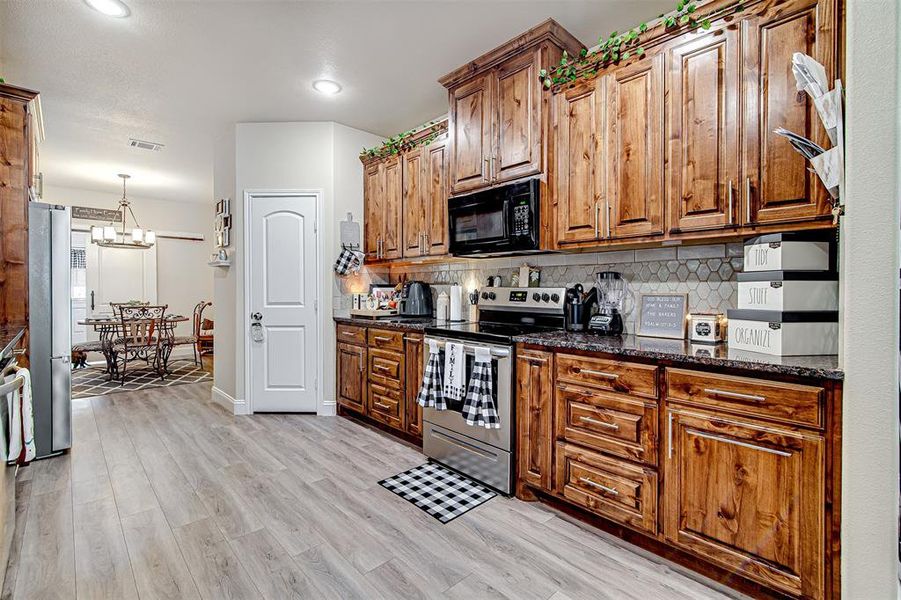 Kitchen with appliances with stainless steel finishes, backsplash, dark stone counters, light hardwood / wood-style flooring, and a chandelier