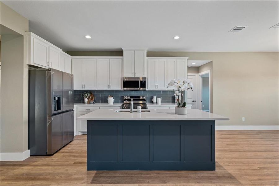 Kitchen with decorative backsplash, appliances with stainless steel finishes, light wood-type flooring, white cabinets, and an island with sink