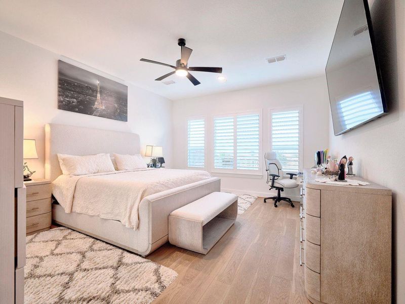 Discover luxury in this spacious primary bedroom with high ceilings, custom wood floors, and expansive windows offering breathtaking views of the yard, trail, and lake. Enhanced with elegant custom shutters.