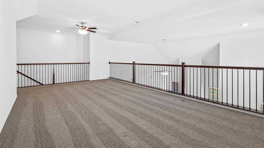 Spacious loft area featuring plush carpet flooring, white walls, and a ceiling fan