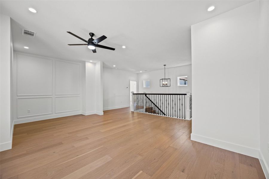 Empty room featuring light wood-style flooring, ceiling fan, and suspended lighting Empty room featuring light wood-style flooring, ceiling fan, and suspended lighting
