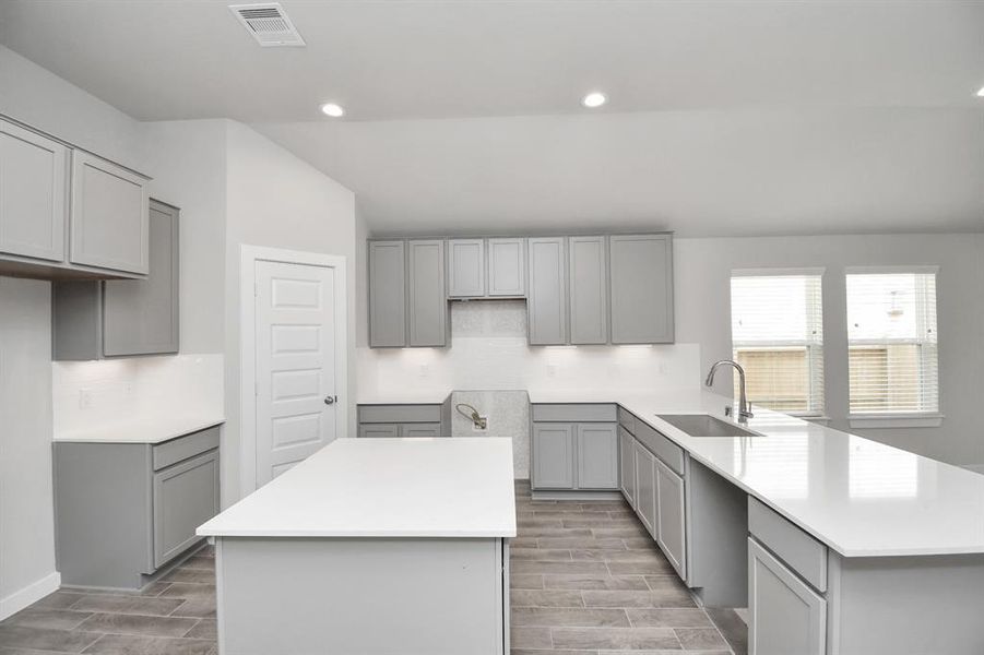 Kitchen features a massive granite island, high ceilings, soft close cabinets, granite countertops, stainless steel appliances (to be installed), a sleek tile backsplash, recessed lighting, and an extended counter area. Sample photo of completed home. Actual color and selections may vary.