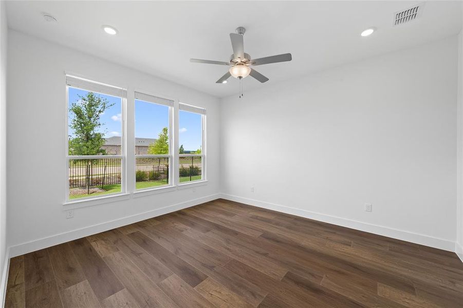 Bright room featuring three large windows, dark wood-finish flooring, recessed lighting, a ceiling fan with light fixture, and white walls with white trim