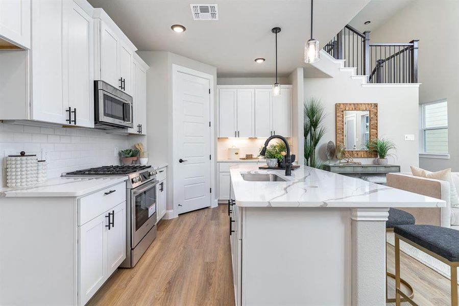 Kitchen featuring appliances with stainless steel finishes, light wood-type flooring, sink, decorative light fixtures, and white cabinetry