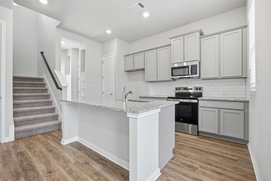 Kitchen featuring gray cabinets, stainless steel appliances, light stone counters, light wood finished floors, and decorative backsplash