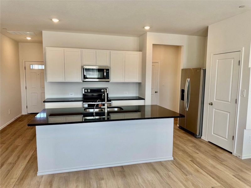 Kitchen with white cabinetry, appliances with stainless steel finishes, a center island with sink, light wood-type flooring, and recessed lighting