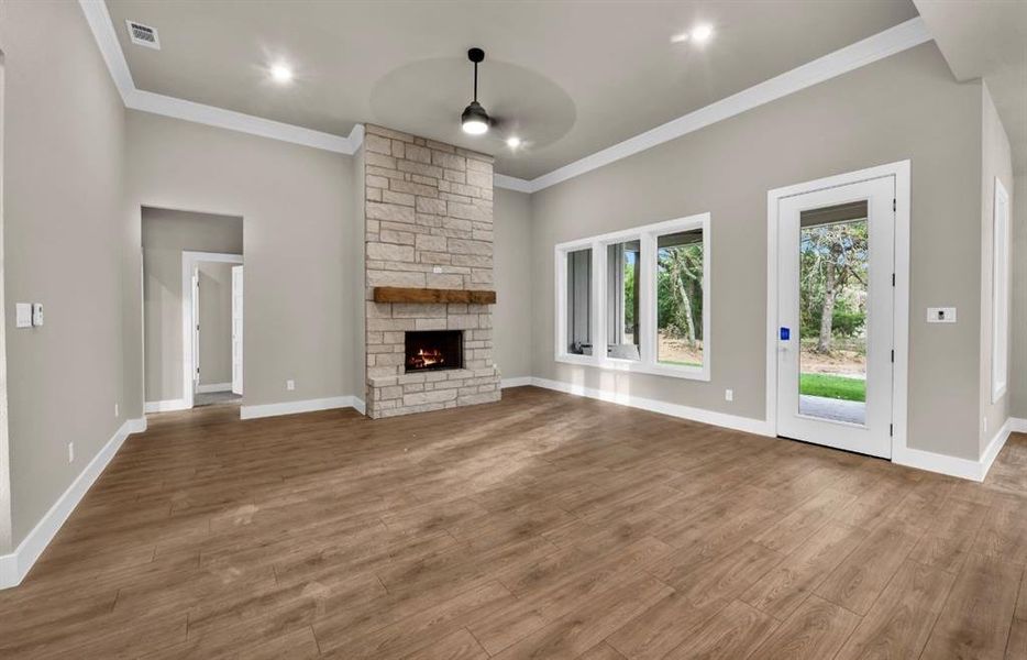 Unfurnished living room with a stone fireplace, wood finished floors, crown molding, recessed lighting, and ceiling fan