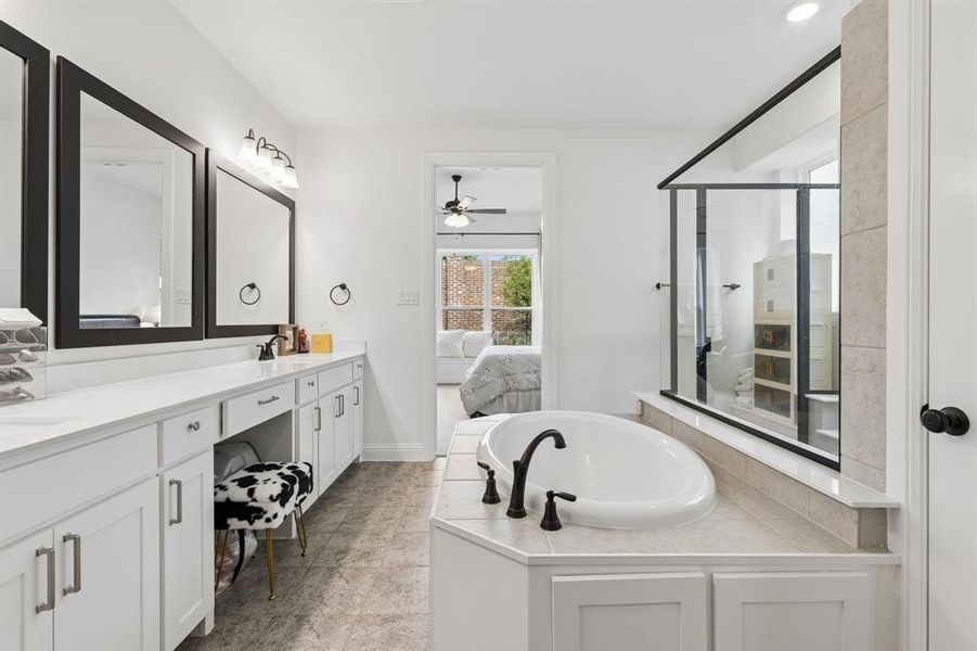 Bright bathroom featuring a built-in soaking tub, a glass-enclosed shower, a double vanity with white cabinetry, and matte black framed mirrors