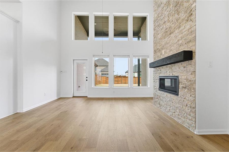 Spacious living area featuring high ceilings, wood-finish flooring, and a stone-clad fireplace with a dark wood mantel