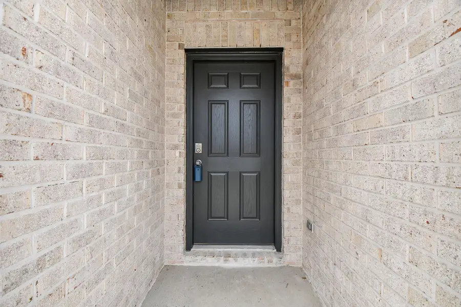 This photo shows a welcoming entryway with a sturdy black front door framed by light brick walls, offering a secure and stylish entrance to the home.