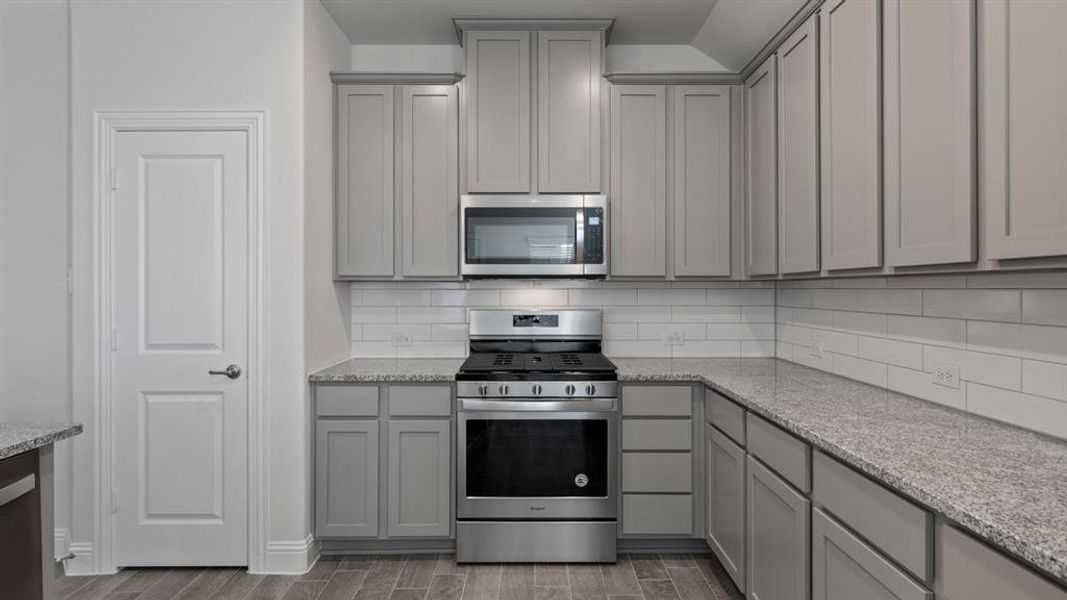 Kitchen featuring gray cabinetry, appliances with stainless steel finishes, light stone counters, backsplash, and wood tiled floors