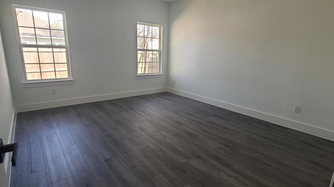 Spacious room featuring wood-finish flooring, two large windows with grid patterns, bright white walls, and substantial baseboards Spacious room featuring wood-finish flooring, two large windows with grid patterns, bright white walls, and substantial baseboards
