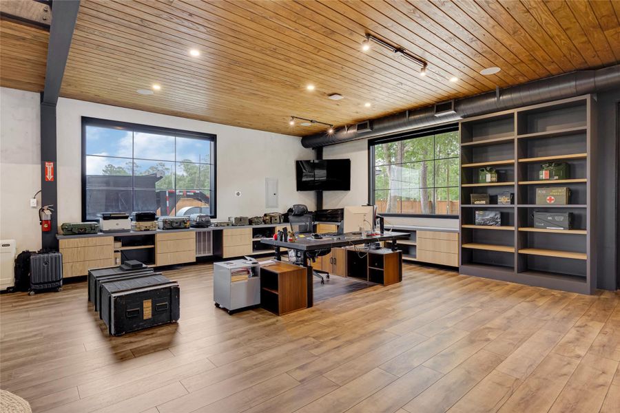 Modern industrial design with a wooden ceiling and floor, ample natural light from large windows, built-in shelves, and a wall-mounted TV. Ideal for a home office or creative studio.