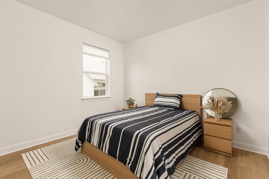 Bright interior space featuring light wood-finish flooring, white baseboards, and a single window with a roller shade