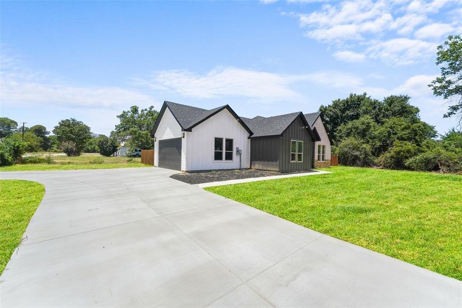 Modern farmhouse exterior featuring white vertical siding, dark gray board and batten accents, a black shingled roof, a concrete driveway, and a manicured lawn Modern farmhouse exterior featuring white vertical siding, dark gray board and batten accents, a black shingled roof, a concrete driveway, and a manicured lawn