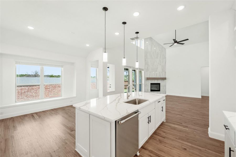 Open kitchen with white island, quartz countertop, and pendant lights, open to living area with marble fireplace and hardwood floors.