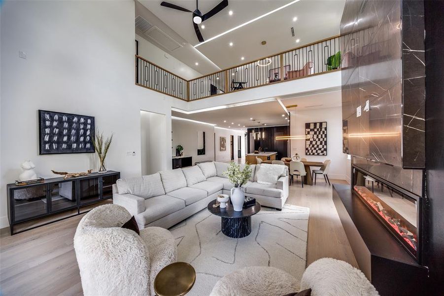 Living room featuring ceiling fan, a towering ceiling, and light hardwood / wood-style flooring