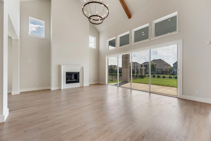 Unfurnished living room featuring high vaulted ceiling, light wood-style floors, a glass covered fireplace, beamed ceiling, and a chandelier Unfurnished living room featuring high vaulted ceiling, light wood-style floors, a glass covered fireplace, beamed ceiling, and a chandelier